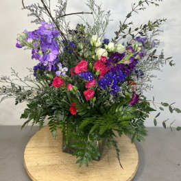 Tall mixed bouquet with purple, pink, and white flowers in a glass vase