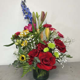 Mixed bouquet of red roses, lilies, and blue delphinium in a glass vase