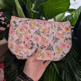 Pink quilted floral pouch held in front of large green houseplant leaves