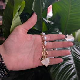 Hand holding a gold heart keychain in front of large green leaves