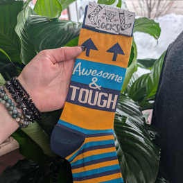 Hand holding a pair of striped novelty socks with "Awesome & Tough" text