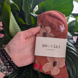 Hand holding folded patterned socks with a mo: vint label