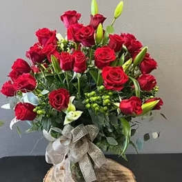 Large arrangement of red roses with white calla lilies and lily buds in a glass vase with burlap bow.