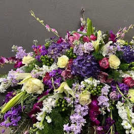 Large low spray of purple, lavender, and white roses, lilies, hydrangeas, and orchids in a dense arrangement