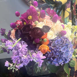 Vibrant mixed bouquet with purple hydrangea, roses, ranunculus and stock in a clear glass cube vase