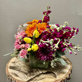 Mixed bouquet in a square glass vase with pink, orange, yellow, and magenta flowers