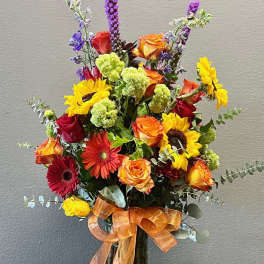 Mixed bouquet with roses, sunflowers, gerbera daisies, and purple spikes in a glass vase
