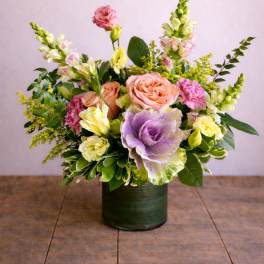 Pastel floral arrangement in a dark green vase with roses and snapdragons