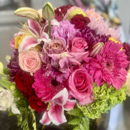 Round bouquet of pink lilies, roses, gerbera daisies, and green hydrangeas in rich pink and red tones