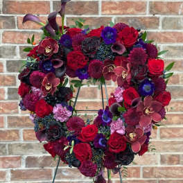 Heart-shaped floral wreath with red, purple, and black blooms on a stand