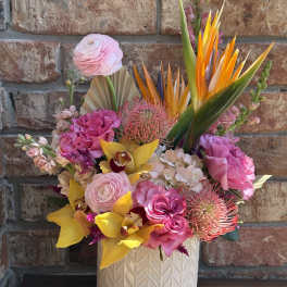 Bright tropical bouquet in a white textured vase with pink and yellow blooms