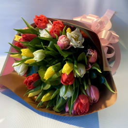 Bouquet of multicolored tulips wrapped in brown paper with a pink ribbon