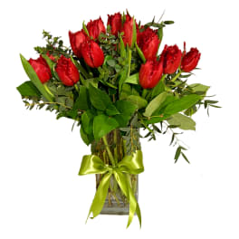 Red tulips arranged in a glass vase with a green ribbon