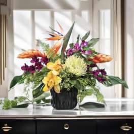 Tropical flower arrangement in a black vase with orange and purple blooms