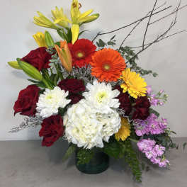 Colorful mixed bouquet with roses, lilies, gerberas, and white hydrangea in a glass vase