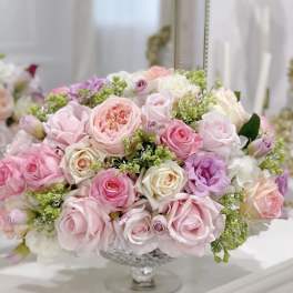 Pastel pink and lavender roses arranged in a clear pedestal vase