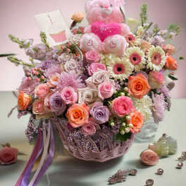 Pink teddy bear in a basket of roses and daisies with a love card