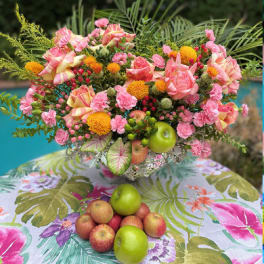 Pink and yellow floral arrangement with apples on a tropical-patterned tablecloth