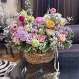 Mixed pastel flower arrangement in a wicker basket with ribbon ties
