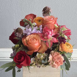 Mixed bouquet of roses, ranunculus, and carnations in a wooden box