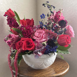 Mixed bouquet of red, pink, and blue flowers in a white bowl vase