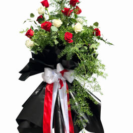 Tall standing arrangement of red and white roses with black wrap and ribbons