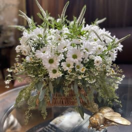 White daisy bouquet in a wicker basket with trailing greenery