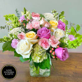 Pastel roses, hydrangea, and mixed blooms arranged in a clear square glass vase