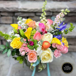 Colorful mixed bouquet of roses, calla lilies, irises and other blooms in a glass vase with ribbon.