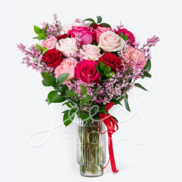 Tall bouquet of red, hot pink, and pale pink roses with tiny pink filler flowers in a clear glass vase with red ribbon.