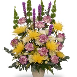 Tall mixed flower arrangement in a beige vase with yellow and purple blooms