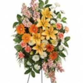 Standing floral spray with yellow lilies, orange daisies, and pink flowers