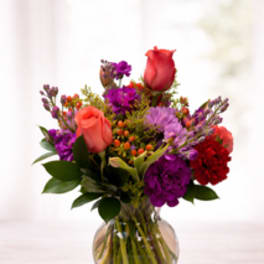 Mixed bouquet of coral roses and purple flowers in a clear glass vase