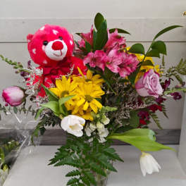 Bouquet of mixed flowers with a pink teddy bear in a glass vase