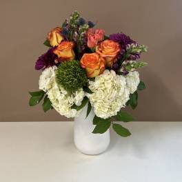Bouquet of orange roses, white hydrangeas, and purple flowers in a white vase