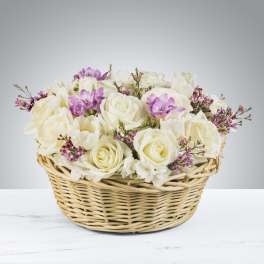 Low basket arrangement of white roses with touches of purple and pink flowers