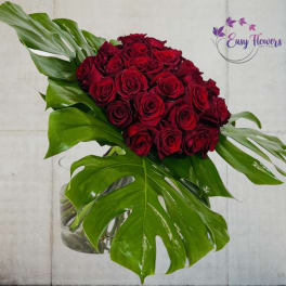 Red rose bouquet with large tropical leaves in a glass vase