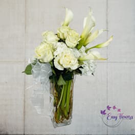 White roses and calla lilies in a clear glass vase with a white ribbon