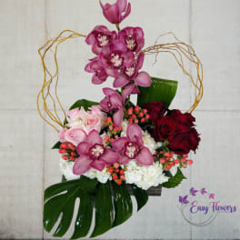 Pink orchids and roses arranged in a decorative basket with large leaves.