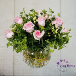 Pink roses arranged in a clear glass vase with greenery