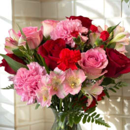 Pink and red bouquet of roses, carnations, and alstroemeria in a glass vase