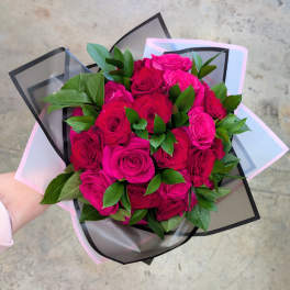 Handheld bouquet of bright pink roses with green foliage in pastel and black wrap
