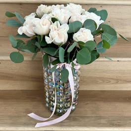 White roses in a mirrored vase with a pink ribbon