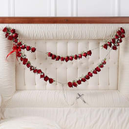 Red rose garlands draped across a white tufted headboard with a small cross pendant