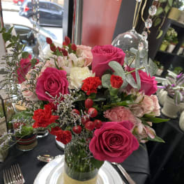 Pink and red rose centerpiece in a glass vase on a set table