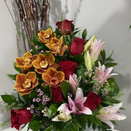 Mixed bouquet of red roses, orchids, and lilies in a black vase