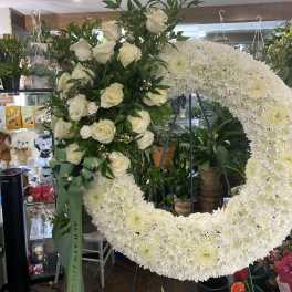 White rose arrangement beside a large white chrysanthemum wreath