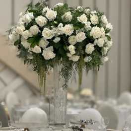 Tall white rose centerpiece in a clear glass vase on a banquet table