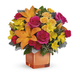 Bright bouquet of roses, lilies, and yellow alstroemeria in an amber glass vase