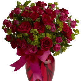 Bouquet of red and pink roses in a red glass vase with a ribbon